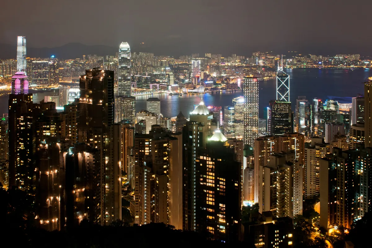 The Central skyline and Victoria Harbour lit at night, seen from the Peak, with high-rise towers in the foreground