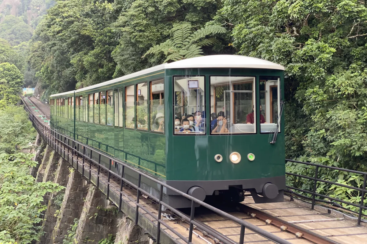 A green Peak Tram car on a stone viaduct above a forested slope